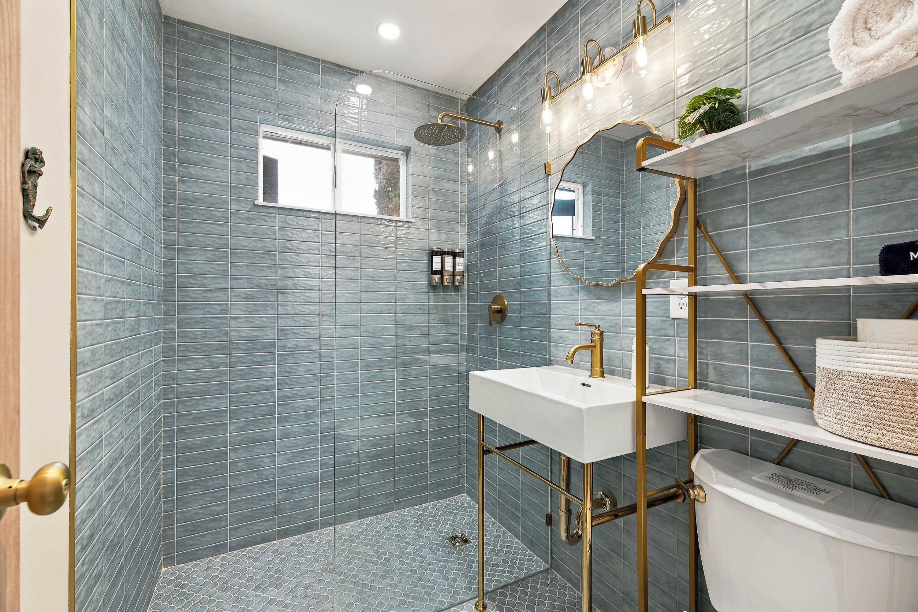 Ein Badezimmer mit blauen Fliesen, einem weißen Waschbecken, einem goldenen Wasserhahn und einer Dusche mit Glastür.
