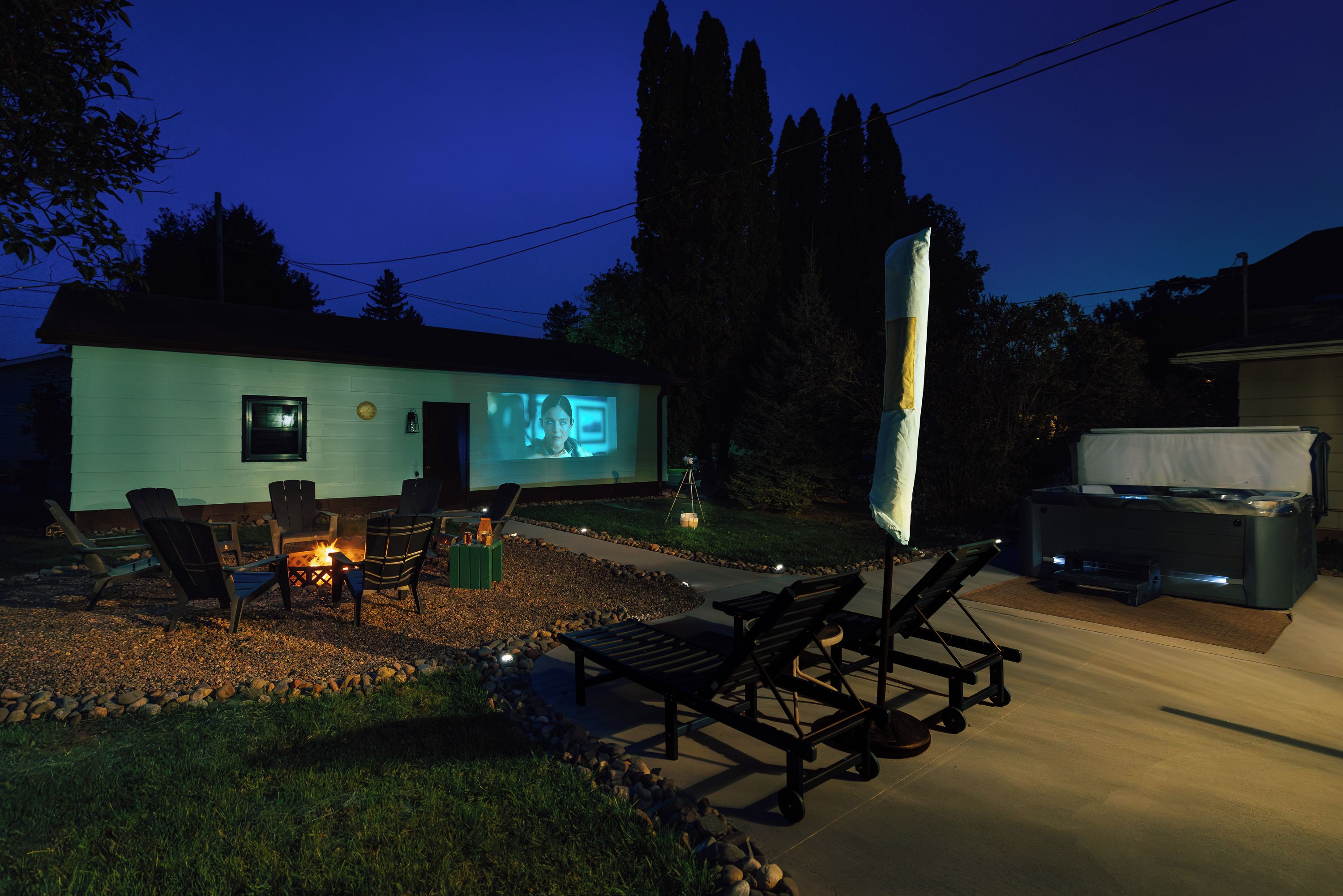 Eine mobile Leinwand für einen Film im Garten mit Feuerstelle, Sitzgelegenheiten und Grill.