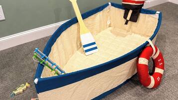 Ein Spielzeugboot mit einem Paddel, einer Rettungsboje und Spielzeugfischen auf einem Teppichboden.