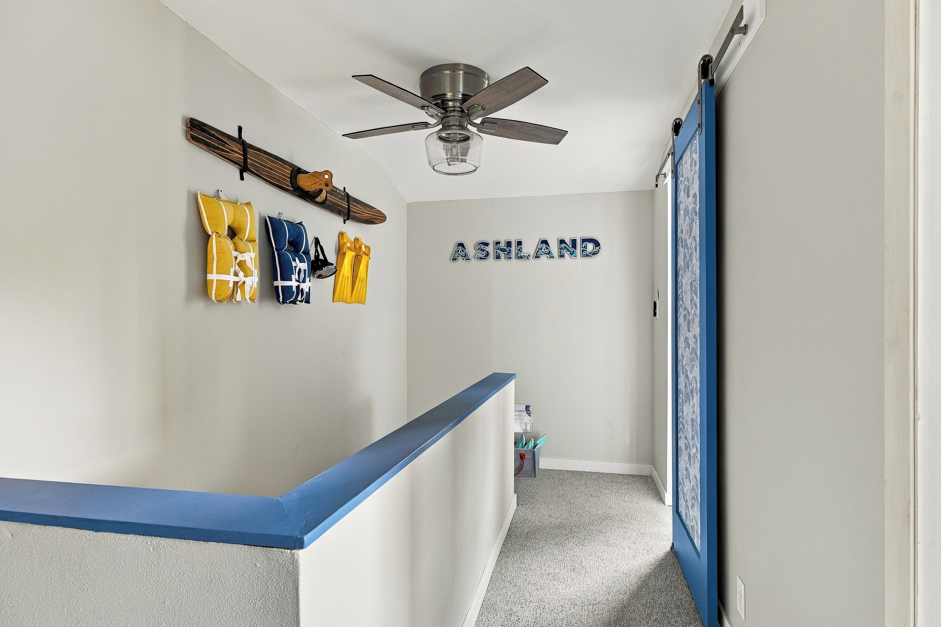 A hallway with a ceiling fan, a wall-mounted sign reading 'ASHLAND,' and a blue railing.