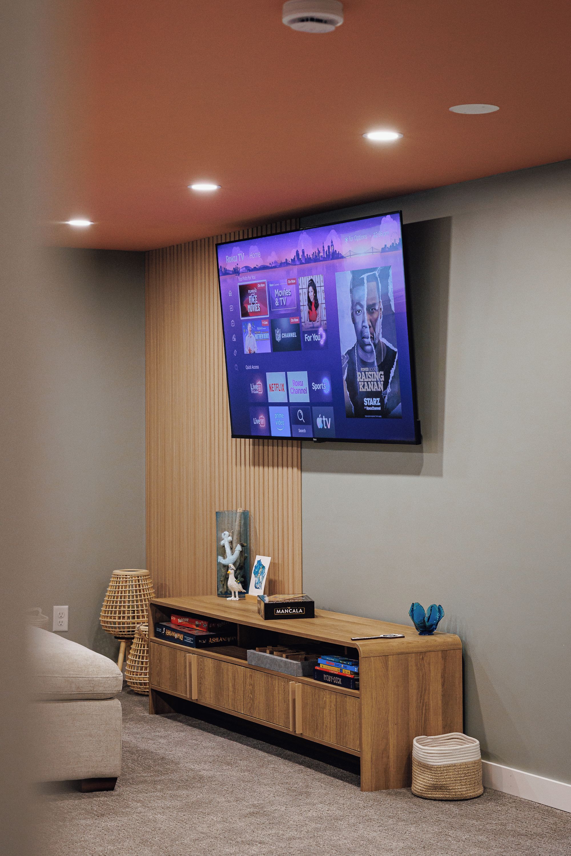 Een moderne woonkamer met een flatscreen televisie aan een houten wand, een houten tv-meubel eronder en een grijs vloerkleed.