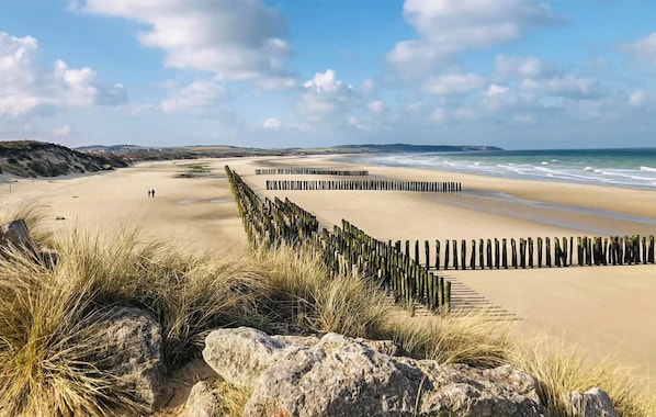 A beach with a wooden fence, sandy dunes, and a clear sky.