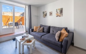 A modern living room with a grey sofa, white coffee table, and two small side tables. There are three wall-mounted artworks above the sofa.