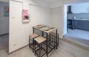 Ein Essbereich mit Tisch für vier Personen, eine Küche im Hintergrund und ein kleines Wandbild.