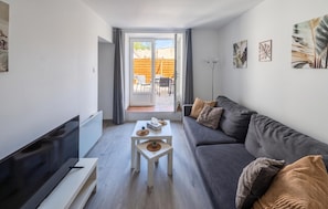 A modern living room with a grey sofa, a flat-screen TV, a small white table with a plant, and a view of an outdoor patio. - Nice home in Ardres with WiFi (Ardres)
