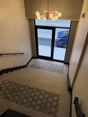 Eine Treppe mit einem gemusterten Teppich, einer Handläufe und einem Blick nach draußen durch eine Tür.