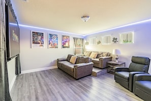 A living room with a sofa set, a coffee table, a TV, and movie posters on the wall. - Magical Disney House-Pool & Hot Tub, Free Waterpark (Davenport)