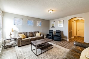 A living room with a brown leather sofa, two black chairs, a coffee table, and a rug. There are three windows with blinds, a lamp on a side table, and framed artwork on the wall. - Magical Disney House-Pool & Hot Tub, Free Waterpark (Davenport)