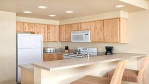 A kitchen with wooden cabinets, a refrigerator, a microwave, a stove, and a coffee maker. - Beachfront WorldMark Seaside Stay with Pools, Space & Family Fun by the Ocean (Seaside)