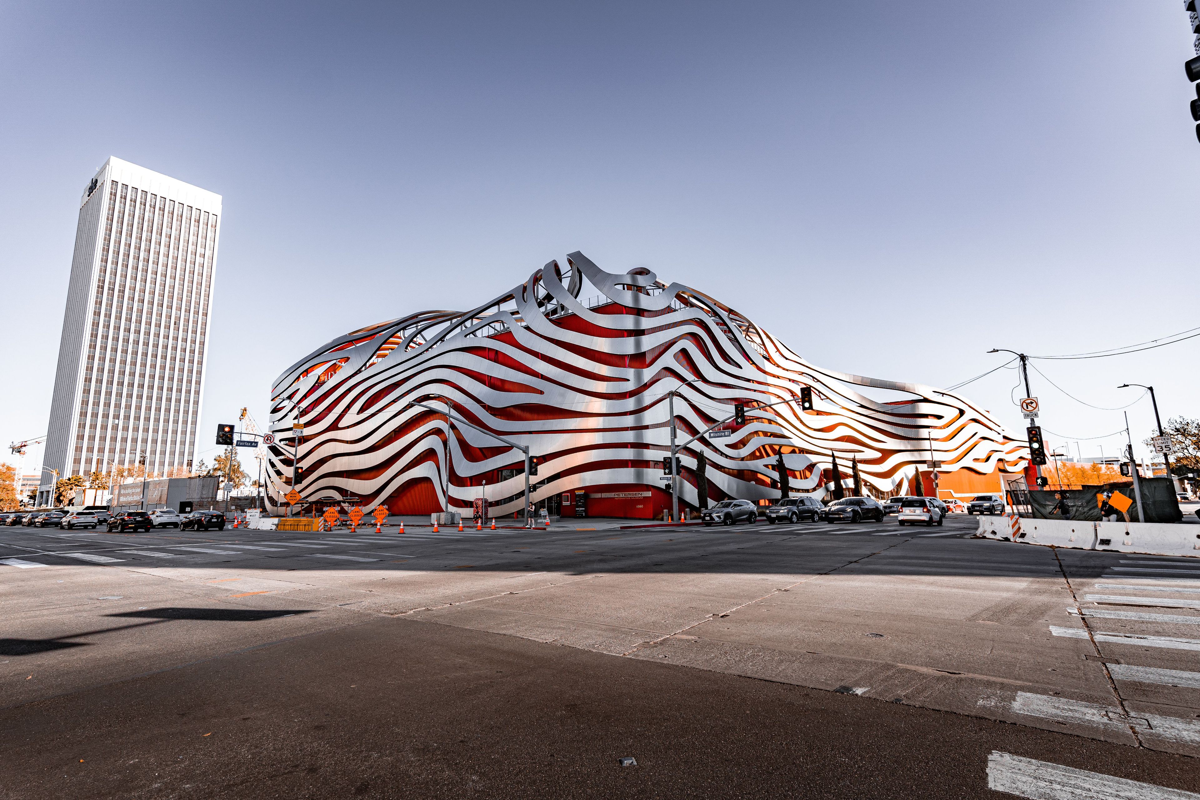 A modern building with a unique wavy facade, located at a street intersection with traffic lights and road signs.