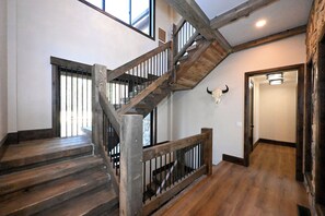 A wooden staircase with a metal railing, a bull skull decoration on the wall, and a door leading to another room. - Misty Mountain Lakefront Lodge with Dock and Hot Tub (Island Park)