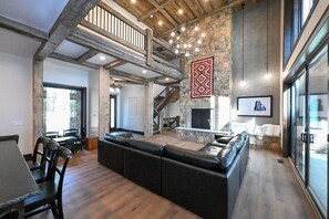 A spacious living area with a large black sectional sofa, a stone fireplace, and a staircase leading to an upper level. - Misty Mountain Lakefront Lodge with Dock and Hot Tub (Island Park)