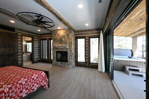 Ein geräumiges Schlafzimmer mit einem großen Bett, einem Kamin aus Stein und Blick auf eine Whirlwanne im Freien.