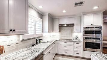 A modern kitchen with white cabinetry, granite countertops, and stainless steel appliances including a double oven and a range hood.