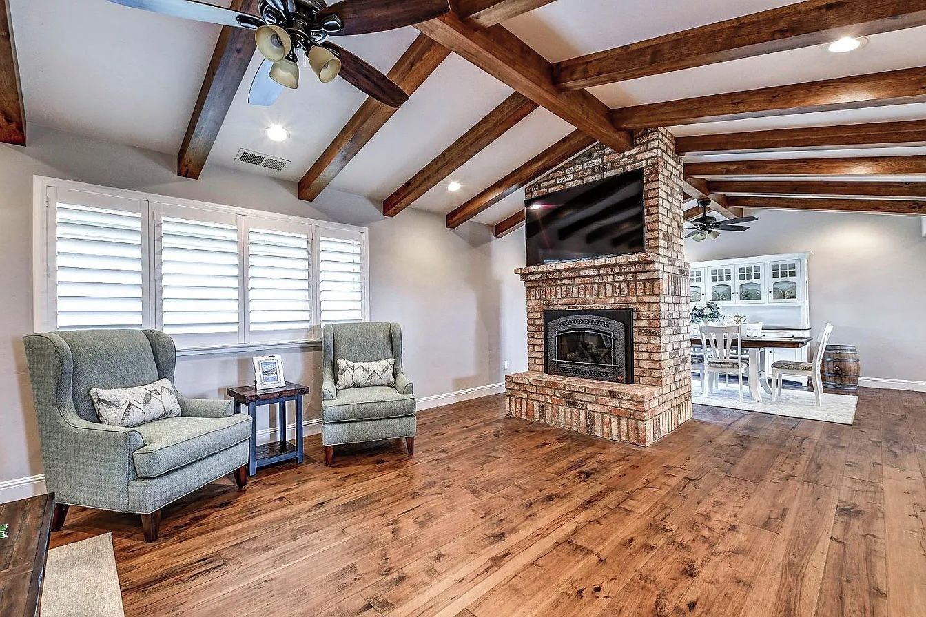 A living room with a fireplace, wooden beams, and a dining area.