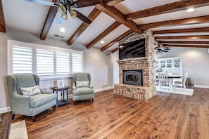 A living room with a fireplace, wooden beams, and a dining area.