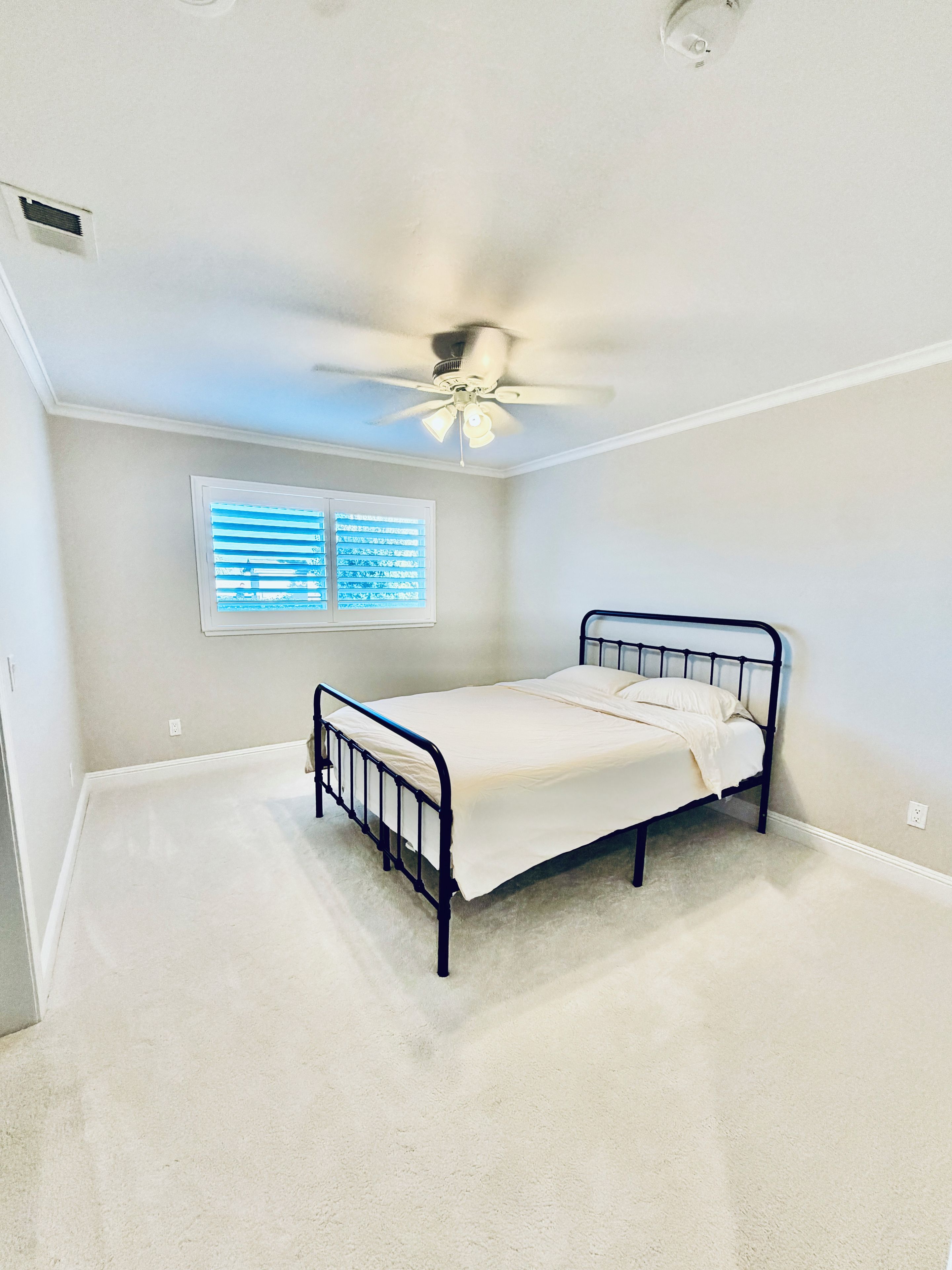 A bedroom with a single bed, a ceiling fan, a window with blinds, and a carpeted floor.