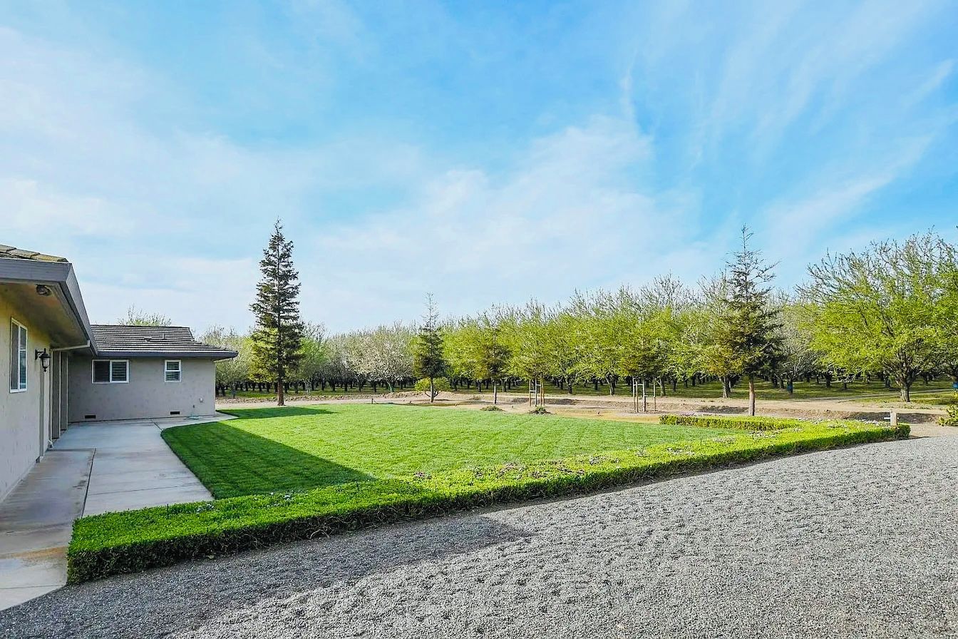 A residential property with a well-maintained lawn, a gravel driveway, and a row of trees.