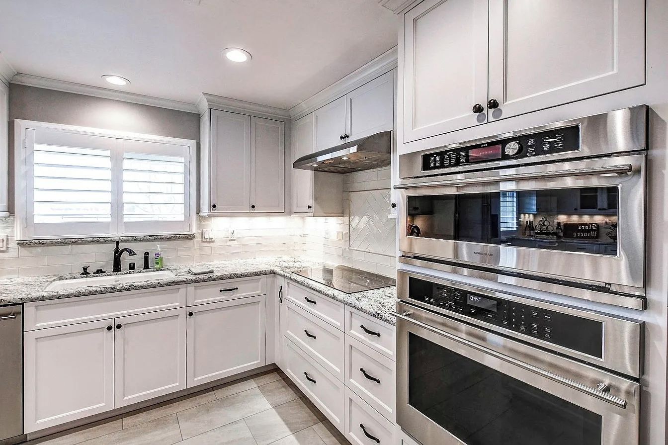 A modern kitchen with stainless steel appliances, white cabinetry, and a granite countertop.