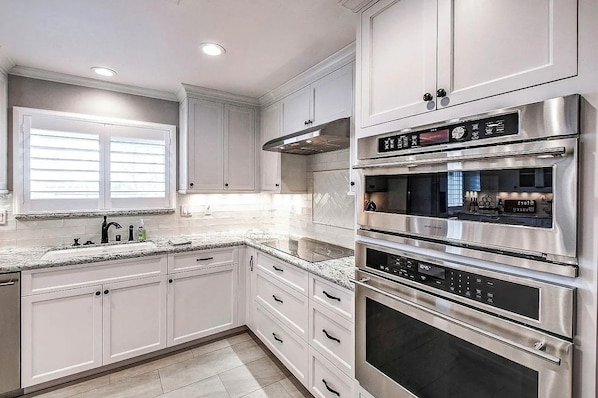 A modern kitchen with stainless steel appliances, white cabinetry, and a granite countertop.