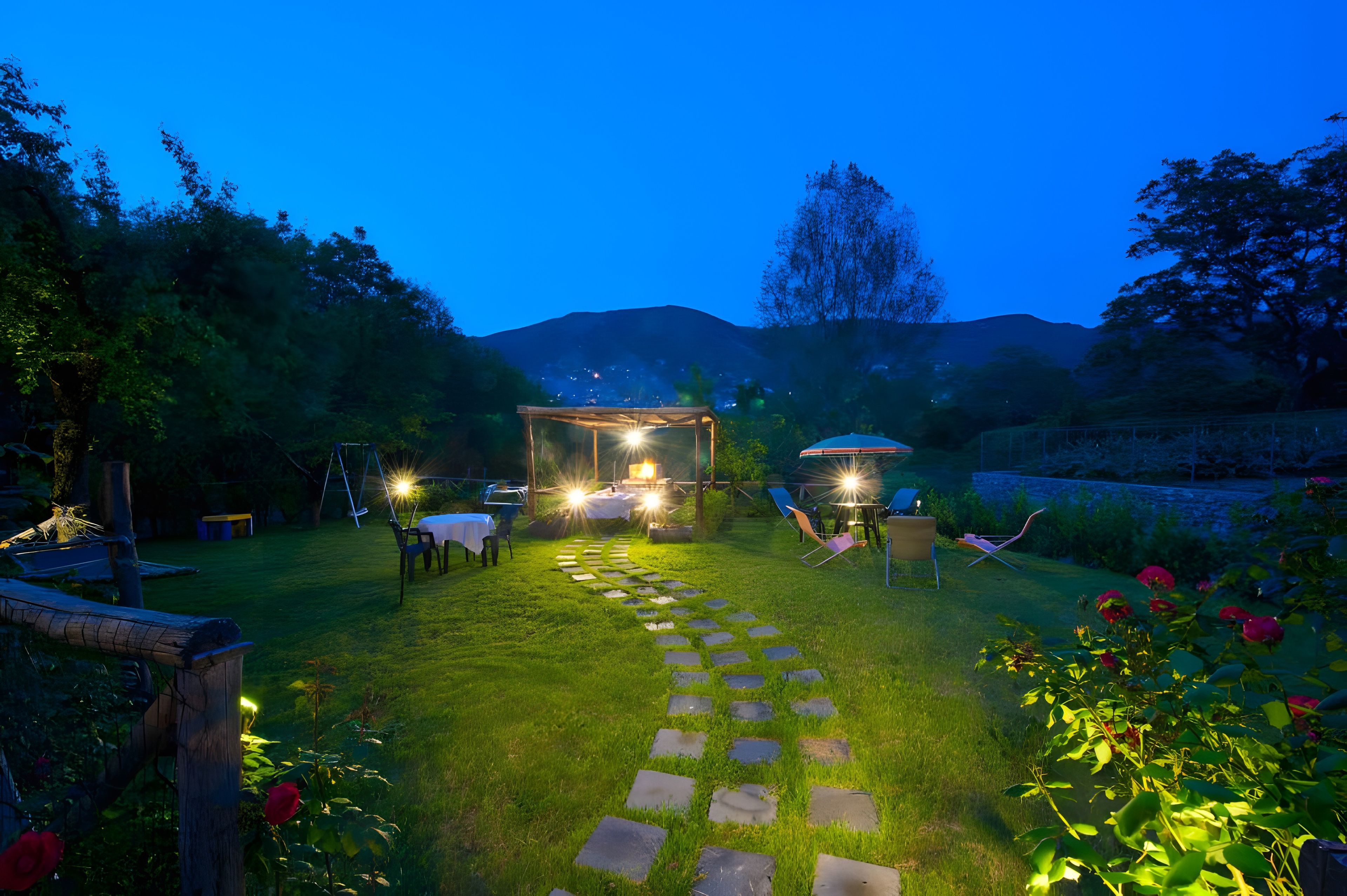 A garden with a stone pathway leading to a seating area with tables and chairs.