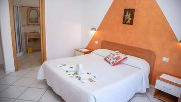 A hotel room with a bed, bedside tables, a nightstand, a mirror, and a bathroom visible through an open door.
