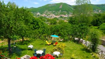 Un jardin luxuriant, avec une grande variété de plantes et de fleurs, un espace aménagé pour pique-niquer avec une table et des chaises, et une vue sur une ville et des collines situées au loin.