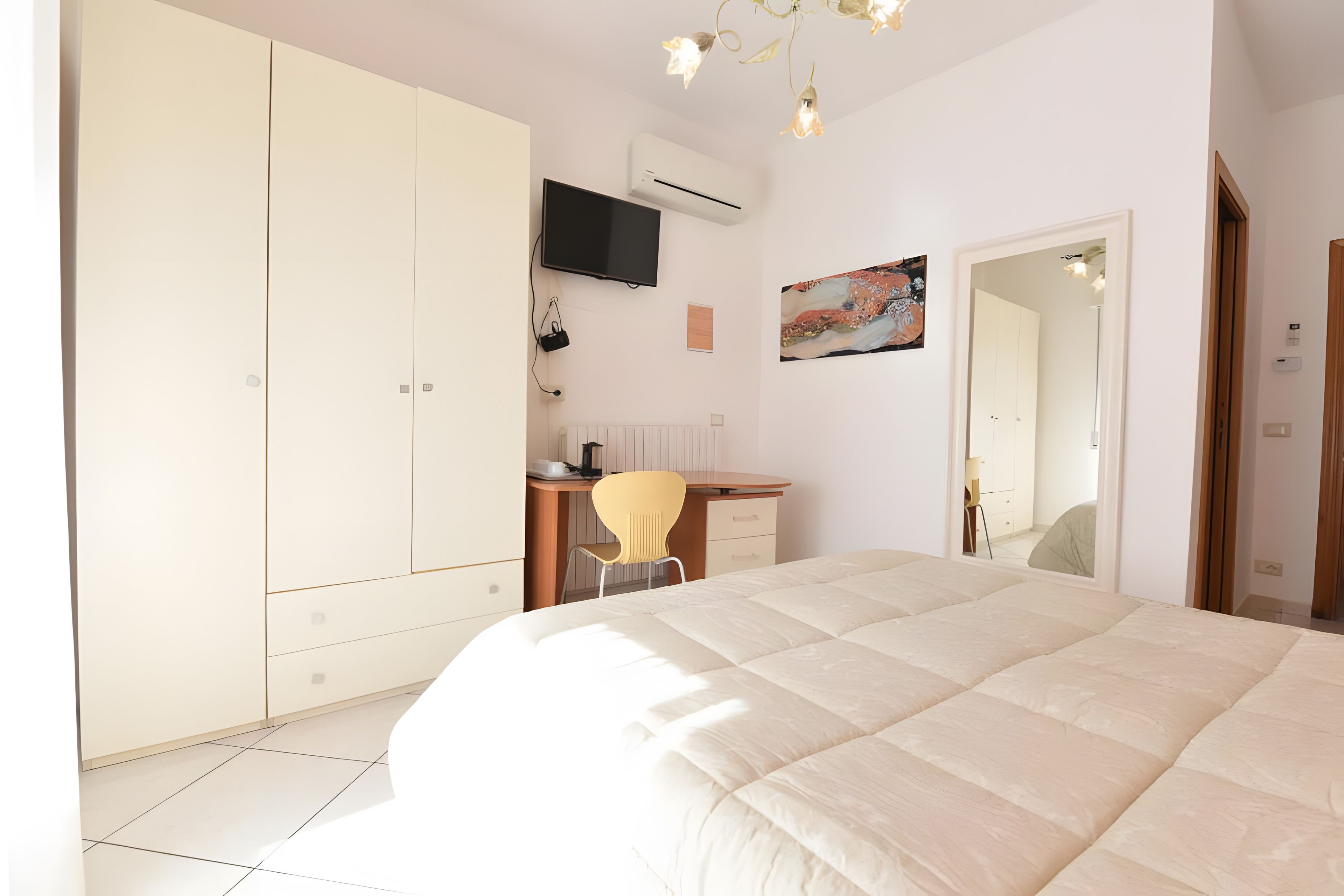A bedroom with a bed, a desk, a chair, a wardrobe, a television, and a painting on the wall.