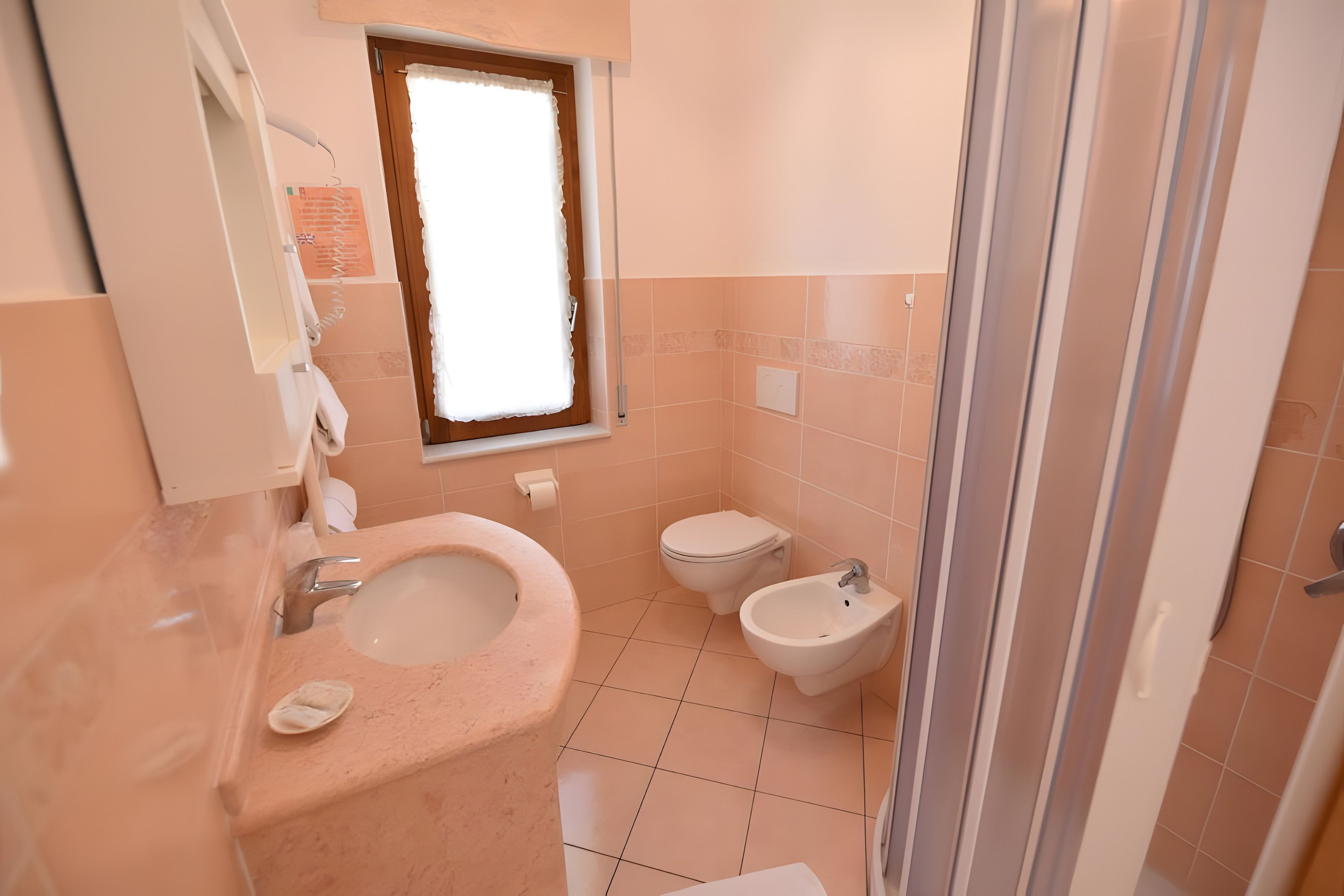 A bathroom with a sink, toilet, bidet, and a window.