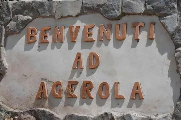 Un letrero de bienvenida con el texto 'BENVENUTI AD AGEROLA' en una pared de piedra.