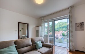 Ein Wohnzimmer mit einer Couch, einem großen Fenster und Blick auf Gebäude und Hügel.
