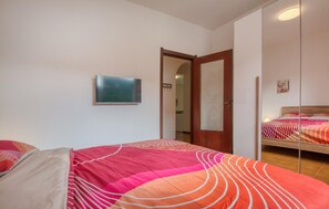 Ein Schlafzimmer mit einem Bett, einem Spiegel, einem Fernseher und einer Tür zu einem weiteren Raum.