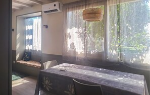 Ein Zimmer mit einem Tisch, bedeckt mit einer blumigen Tischdecke, einem Fenster mit Blick auf Grünflächen und einer Klimaanlage an der Wand.