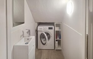 Ein kleines Badezimmer mit einer Waschmaschine von Bosch, einem Waschbecken und einem Spiegel.