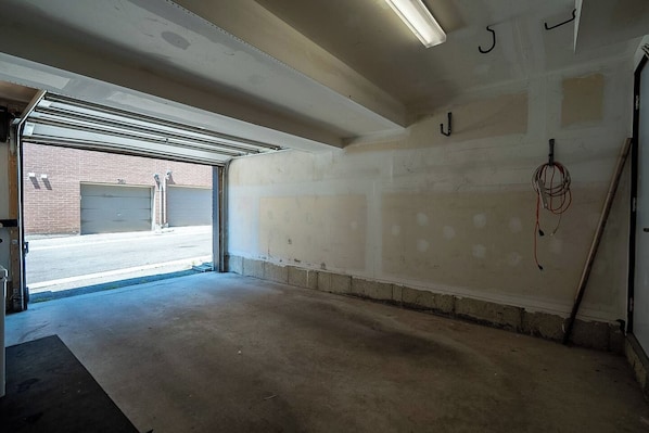 A garage with a concrete floor, a partially finished wall, and a visible garage door. - Modern 4BR Townhome | Rooftop Terraces | Downsview (Toronto)