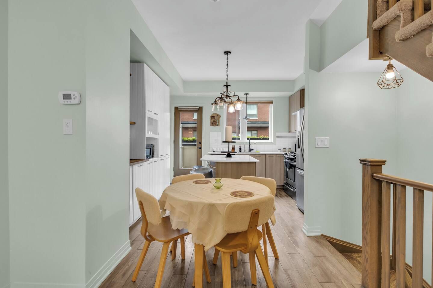A modern kitchen with a dining area, wooden flooring, and a chandelier.