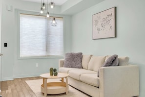 A living room with a beige sofa, a round wooden coffee table, and a cactus on the table. - Modern 4BR Townhome | Rooftop Terraces | Downsview (Toronto)