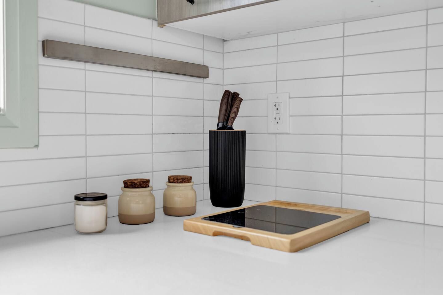 A kitchen with white tiled walls, a black vase with a handle, and three jars with lids.