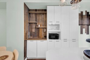 A kitchen with white cabinetry, a wooden accent wall, and a black microwave.