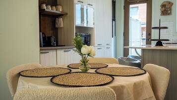 A dining table with placemats, a vase with flowers, and a kitchen in the background.