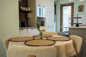 A dining table with placemats, a vase with flowers, and a kitchen in the background.
