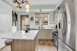 A modern kitchen with a central island, stainless steel appliances, and a hanging light fixture. - Modern 4BR Townhome | Rooftop Terraces | Downsview (Toronto)