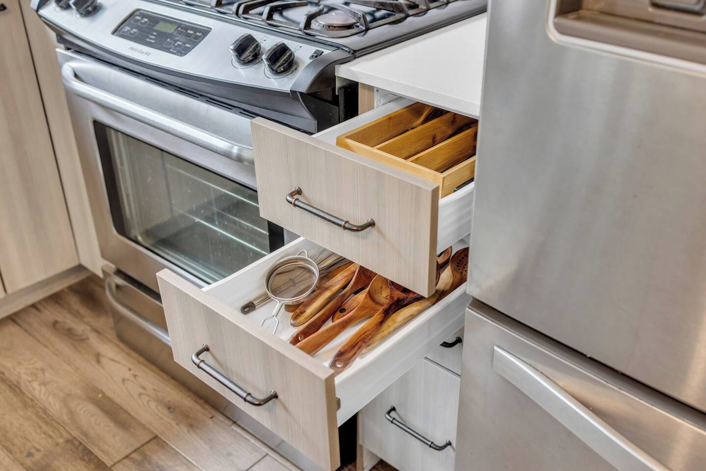 A kitchen with a stainless steel stove, a microwave, and wooden utensils in drawers.