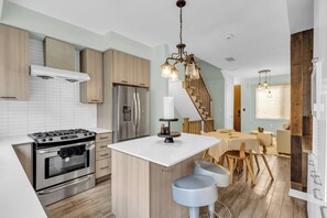 A modern kitchen with a central island, stainless steel appliances, and a wooden staircase.