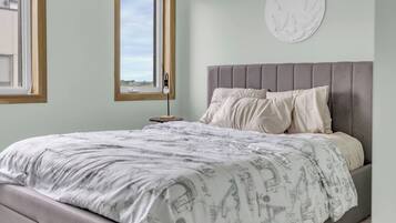 A bedroom with a bed, a nightstand, a lamp, and a window.