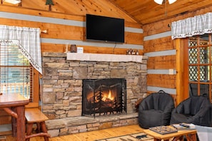 Ein Interieur einer Holzhütte mit Kamin aus Stein, Holzwänden, einem Fernseher und einem Essbereich.