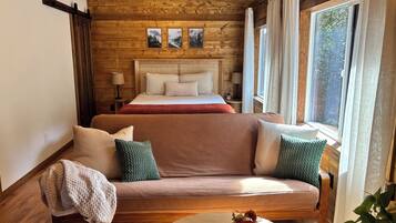 A cozy room with a bed, a sofa, a window with curtains, and a wall with framed pictures.