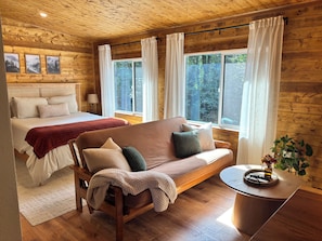 Interior acogedor de una cabaña con cama, sofá y una mesita con una planta.