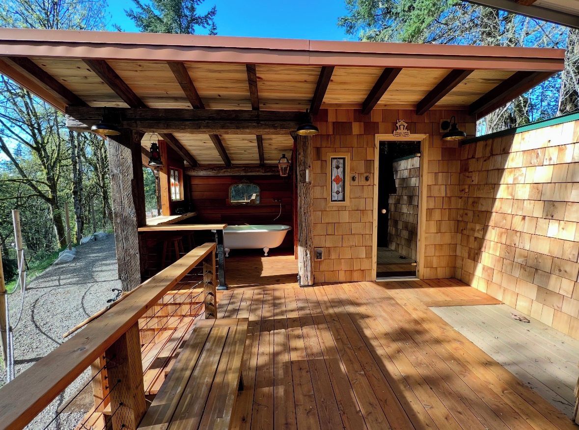 A wooden cabin with a deck, a bathtub, and a door leading to the interior.