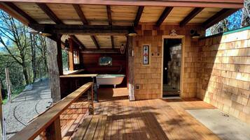 A wooden cabin with a deck, a bathtub, and a door leading to the interior.